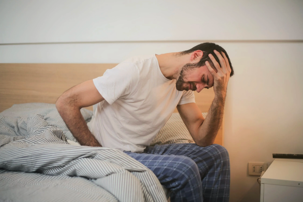 man sitting on the edge of his mattress with head in hand